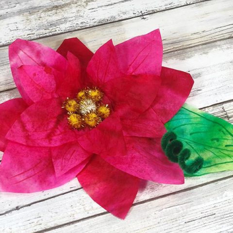 One poinsettia flower made with coffee filters on a white wood background.