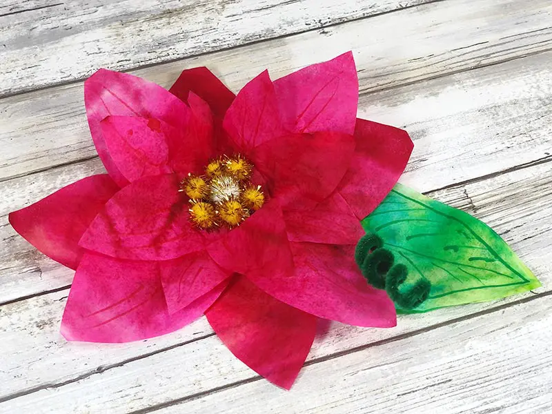 One poinsettia flower made with coffee filters on a white wood background.