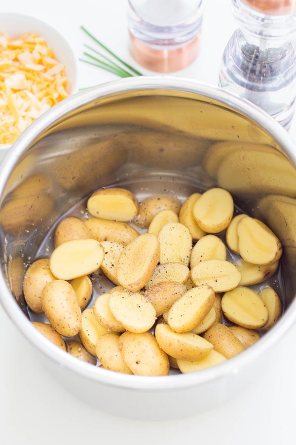Halved potatoes seasoned with salt and pepper in water in silver pot for pressure cooker.