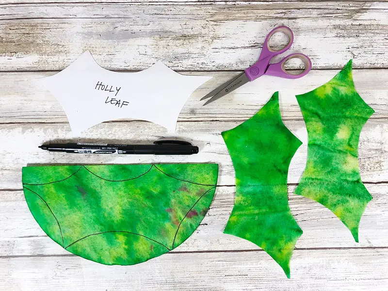 Green coffee filters cut in shape of holly leaves using paper template.