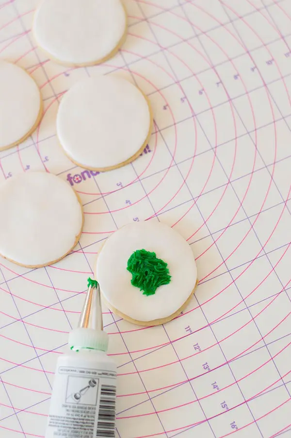 Round sugar cookies covered with white fondant. Green frosting creating tree in center of one.