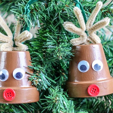 Two completed reindeer clay pot crafts hanging from small tabletop Christmas tree.