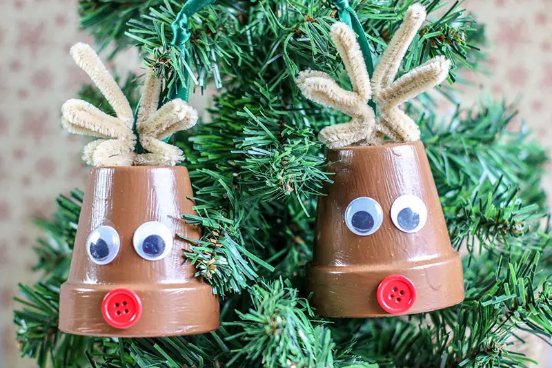 Two completed reindeer clay pot crafts hanging from small tabletop Christmas tree.