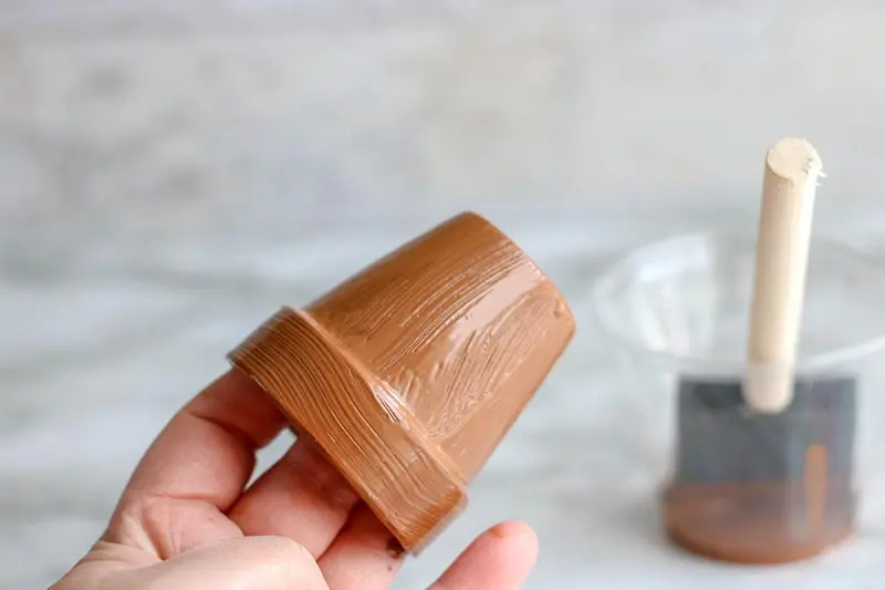 Hand holding small clay flower pot painted brown.