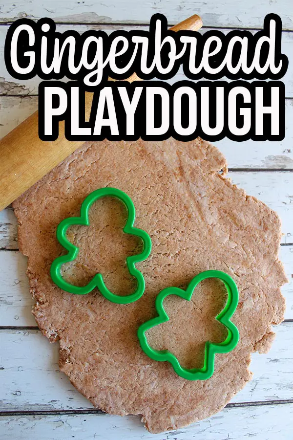 Light brown gingerbread playdough rolled out flat. Rolling pin laying across top of playdough with gingerbread boy and girl cookie cutters on top of dough.