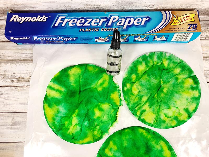 Three coffee filters colored with green and yellow markers set on freezer paper and sprayed with water.