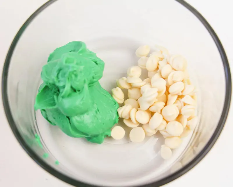 Green frosting and white chocolate chips in glass bowl.