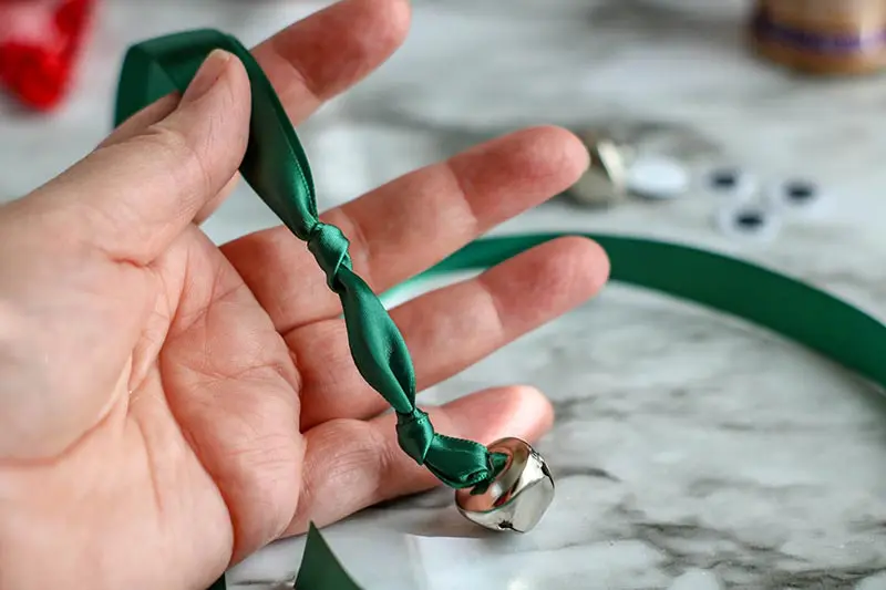 Hand holding green ribbon knotted twice with jingle bell.