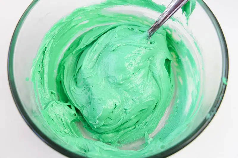 Melted chocolate mixed with green frosting in glass bowl.