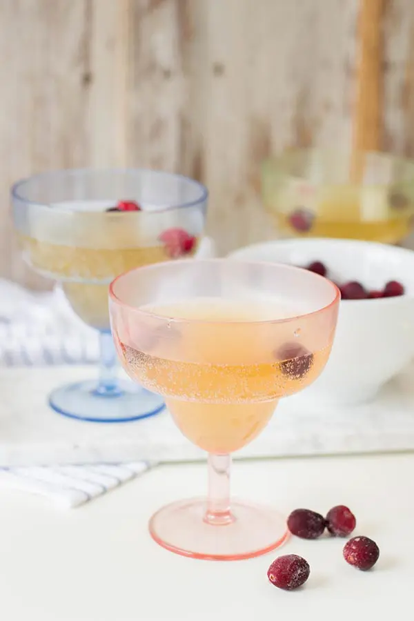 Two cocktail glasses with sparkling pineapple drink and frozen fruit on a white counter.