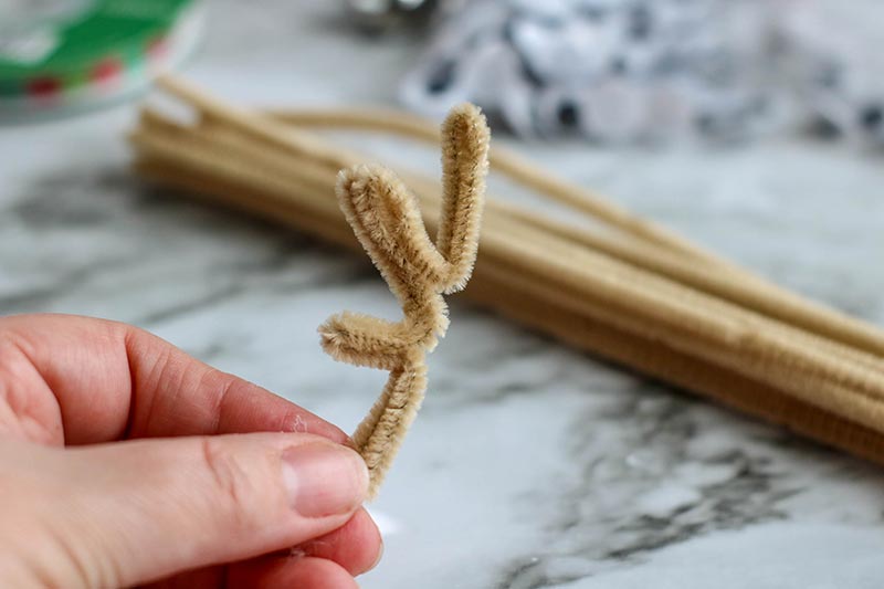 Hand holding beige pipe cleaner folded and bent into antler shape.