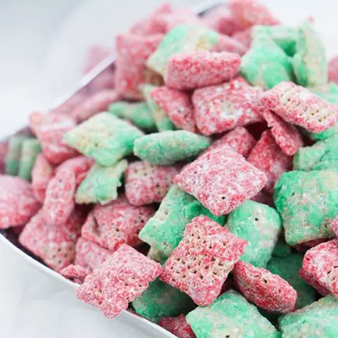 Close view of red and green Christmas puppy chow mix in square silver bowl on white table.