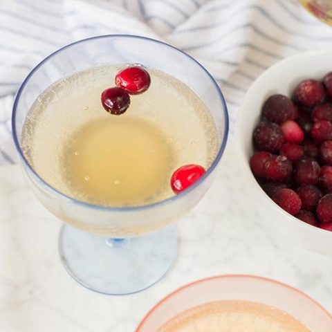 Overhead view of non alcoholic pineapple cocktail with frozen cranberries served in cocktail glasses next to bowl of frozen cranberries.