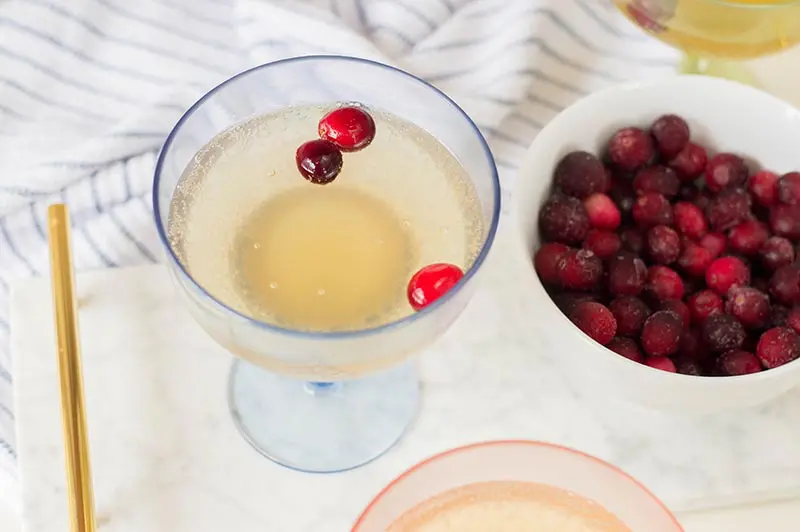 Overhead view of non alcoholic pineapple cocktail with frozen cranberries served in cocktail glasses next to bowl of frozen cranberries.