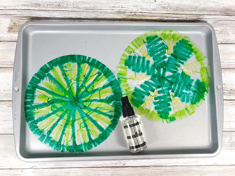 Two coffee filters colored with green marker laying on cookie sheet with a water bottle.