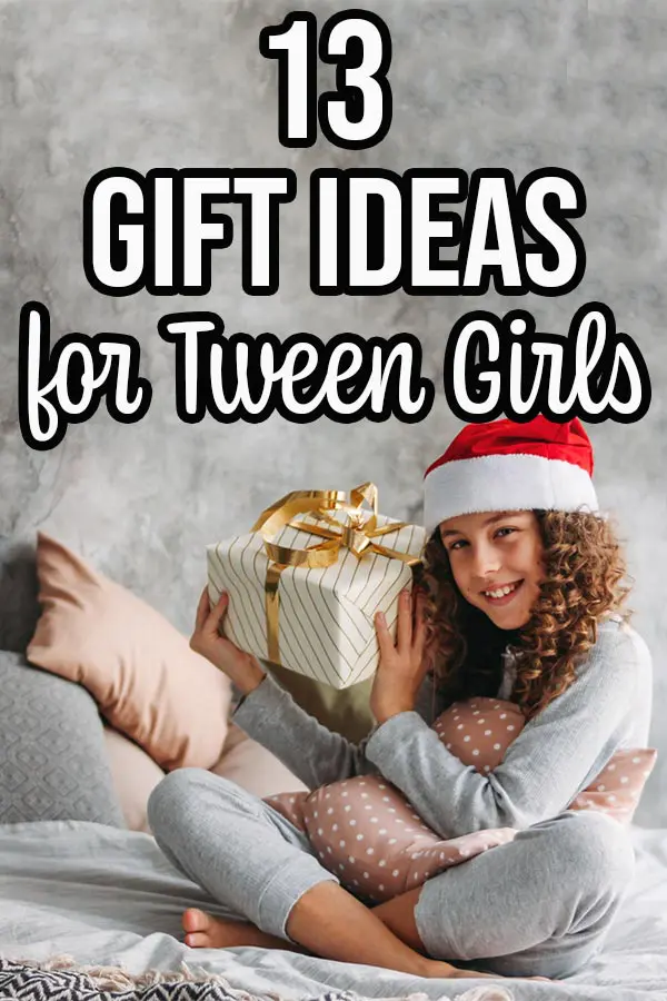 Tween girl sitting on bed holding wrapped present and wearing a Santa hat.