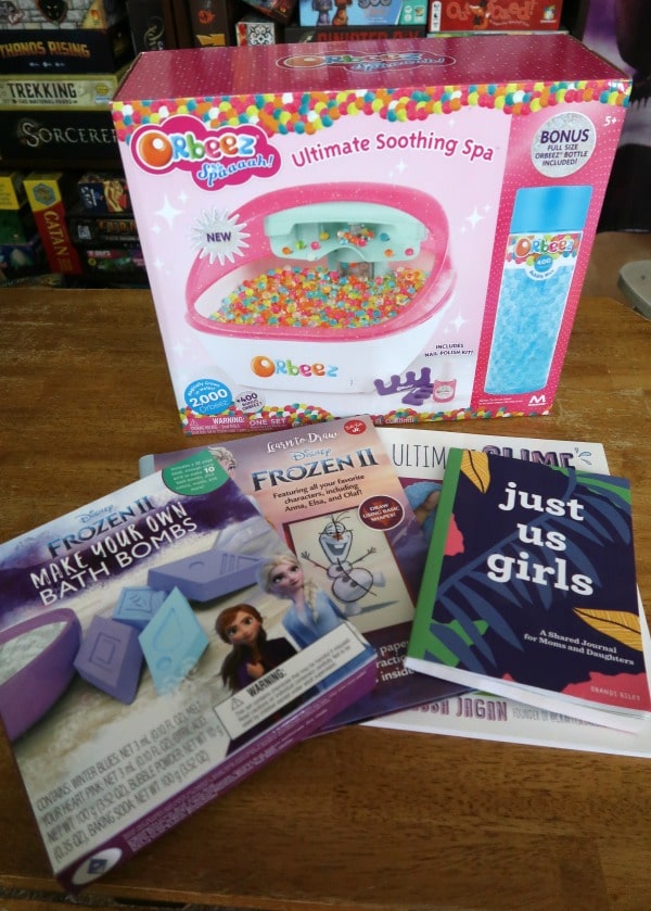 Orbeez foot spa, bath bomb kit, slime book, and mother daughter journal laid out on wooden table.