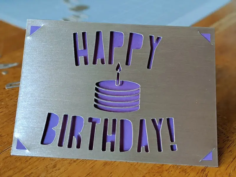 Silver and purple card with Happy Birthday and a small cake cut out of the front.