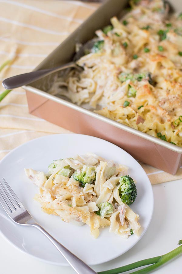 Tuna casserole on small white plate with fork next to baking pan of more.