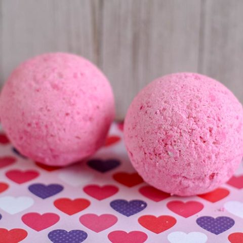 Two round homemade pink bath bombs beside each other on top of heart paper.