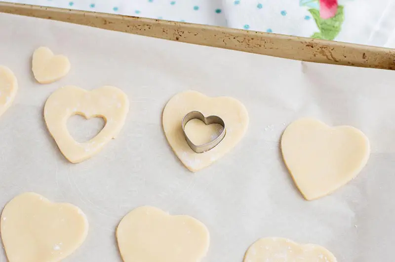 Using small heart cookie cutter to remove inside part of sugar cookies.