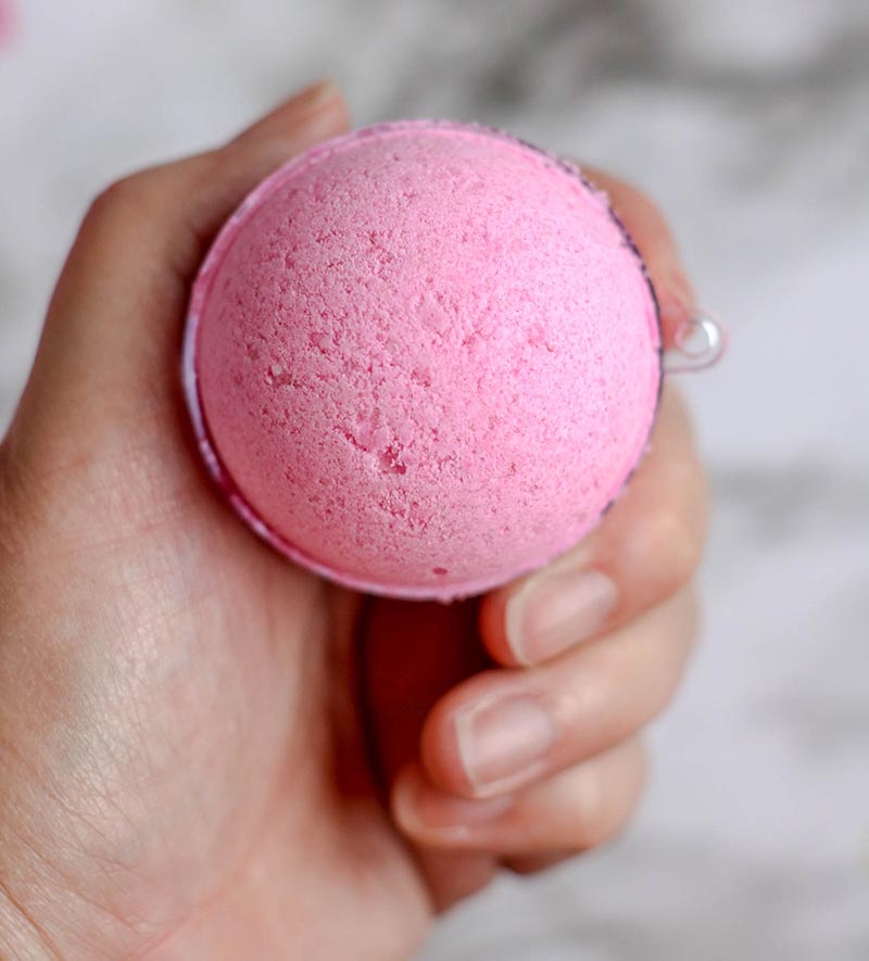 Woman's hand holding finished pink bath bomb.