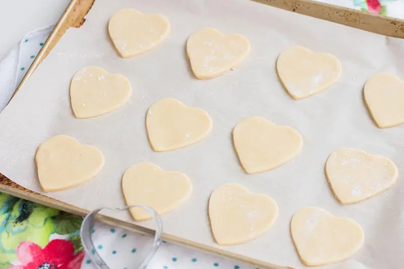 One dozen cut out heart sugar cookies on lined baking sheet before baking.