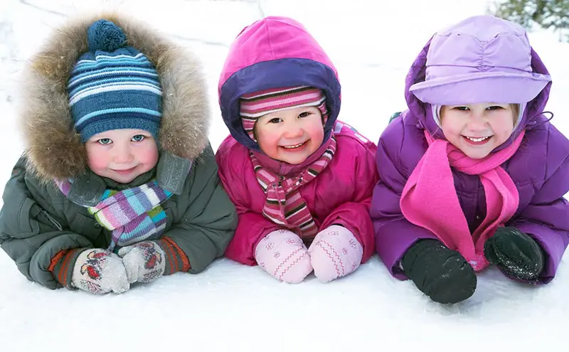 Three little kids laying on the snow and wearing outdoor winter gear.