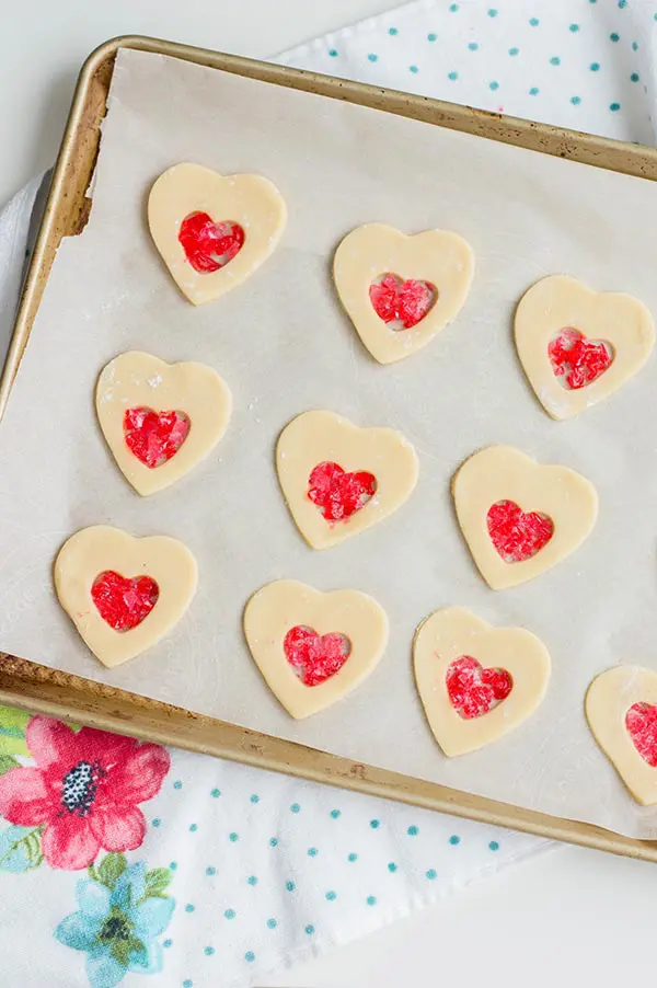 Heart sugar cookie cut outs on baking sheet with crushed candy in center.