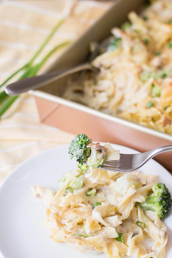 Small white plate with a fork full of tuna noodle casserole in front of casserole serving dish.