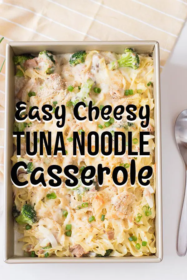 Overhead view of full baking pan with cheesy tuna noodle casserole with serving spoon laying next to it and light yellow cloth. Text overlay with recipe name.