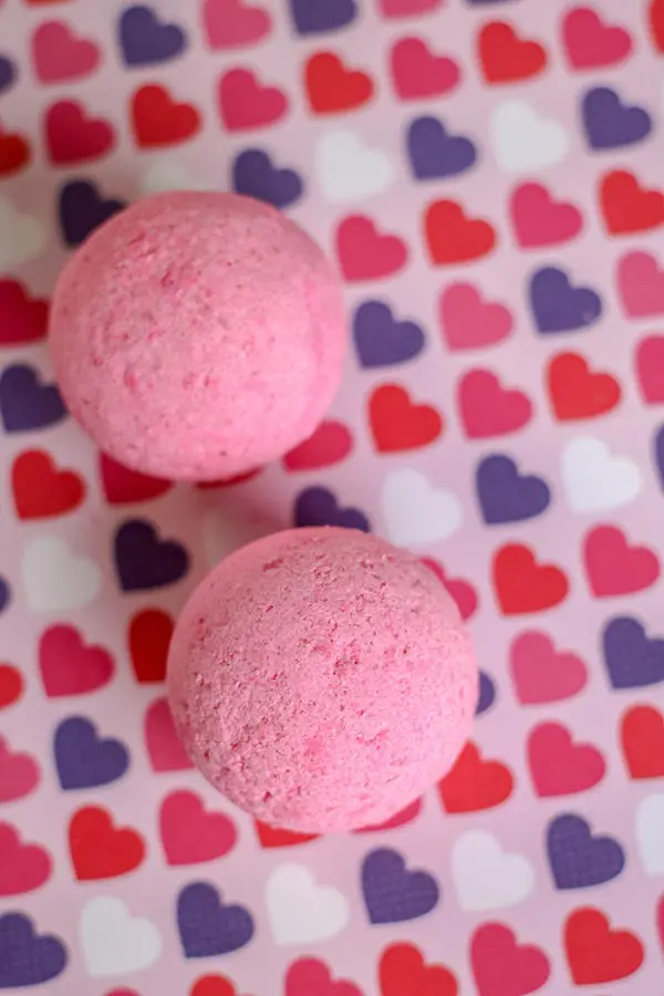 Overhead view of two round pink bath bombs on multi-colored heart paper.