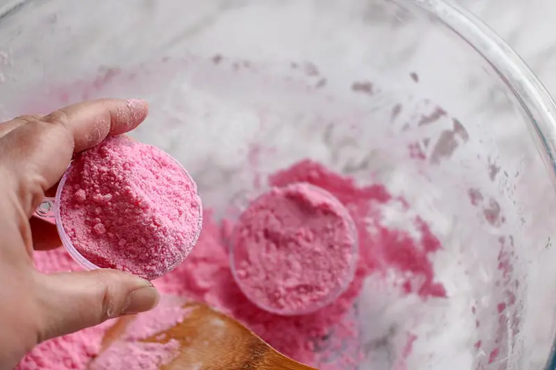 Hand holding one half of bath bomb mold. Pink bath bomb mixture being added to both sides of mold.