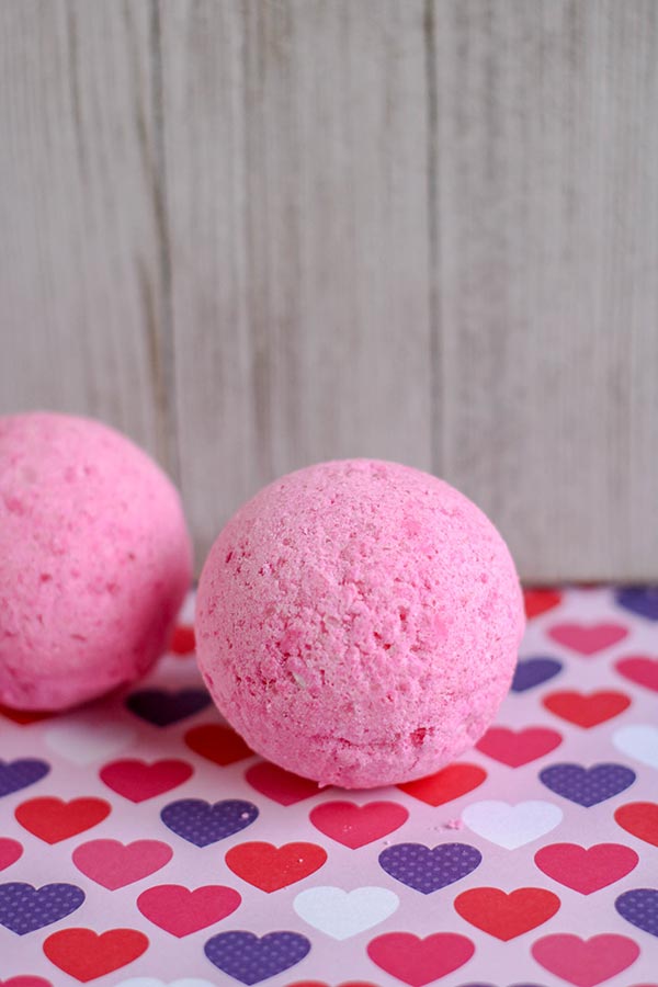 Two completed pink bath bombs sitting on paper with different colored hearts.