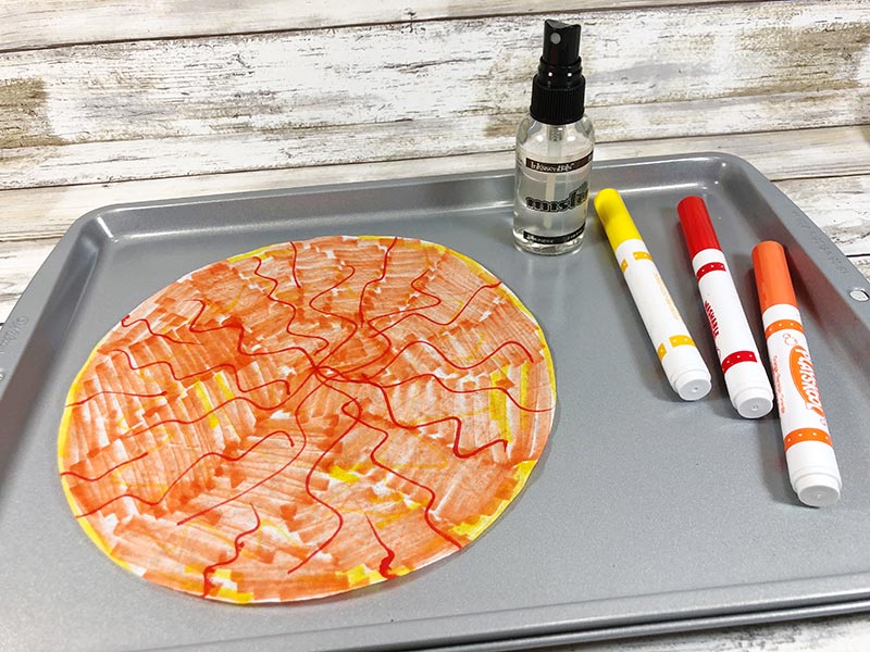 Coffee filter colored with orange, red, and yellow markers laying on cookie sheet.