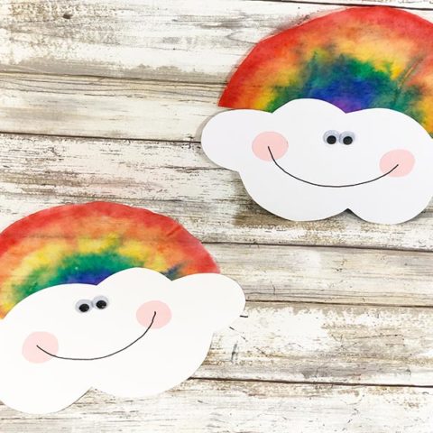 Two coffee filter rainbows with smiling clouds laying on white wood photo background.