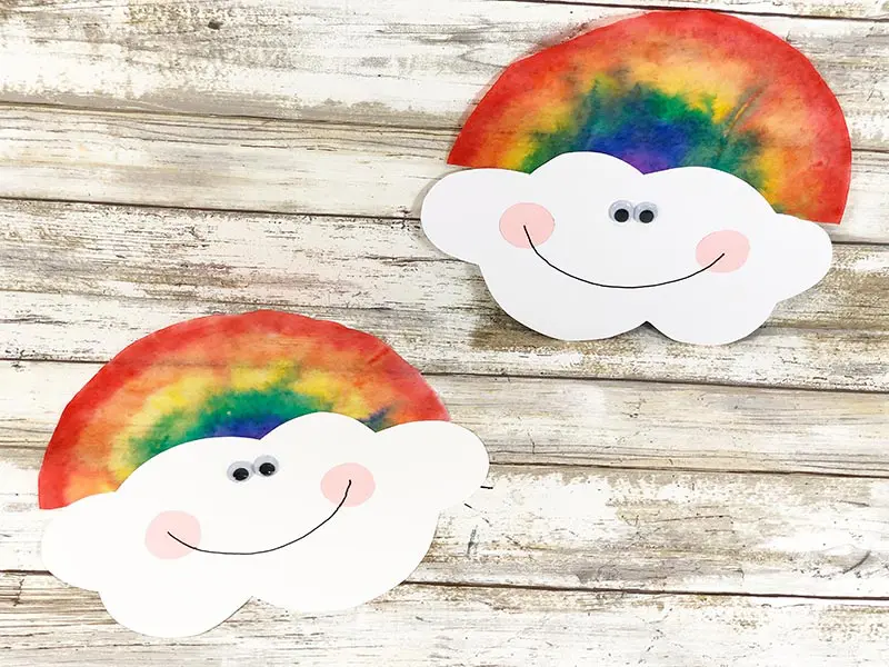 Two coffee filter rainbows with smiling clouds laying on white wood photo background.