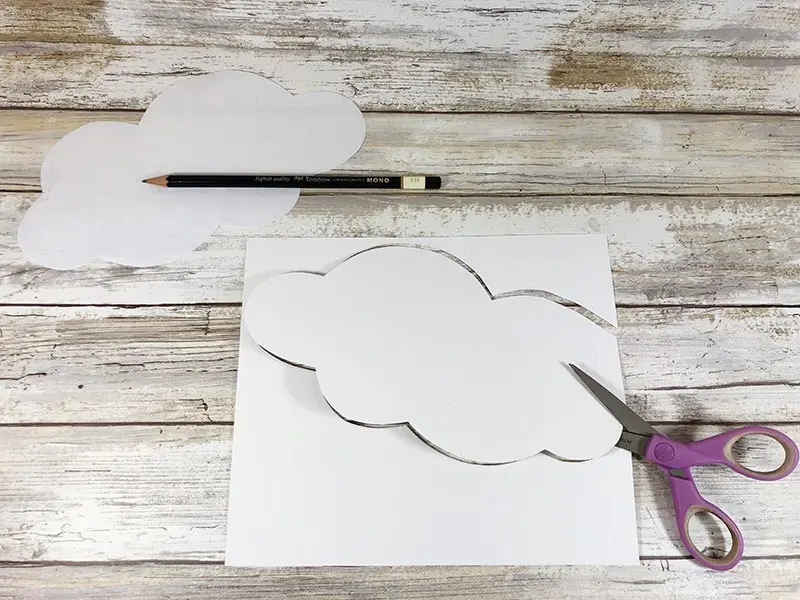 One paper cloud cut out of white paper and another traced and getting cut out.