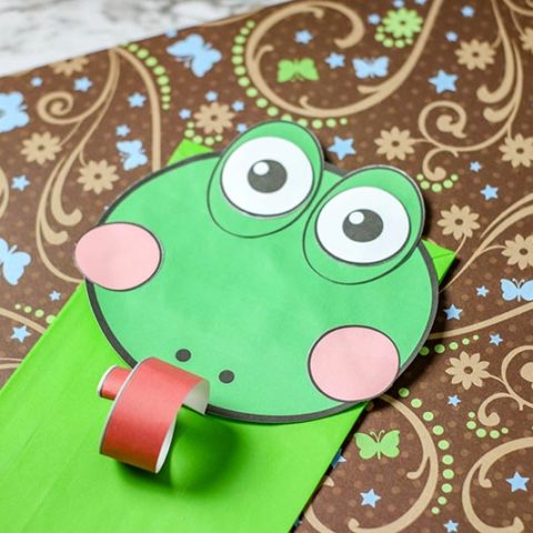 Closer view of paper bag frog puppet using paper cut outs for face and green bag.