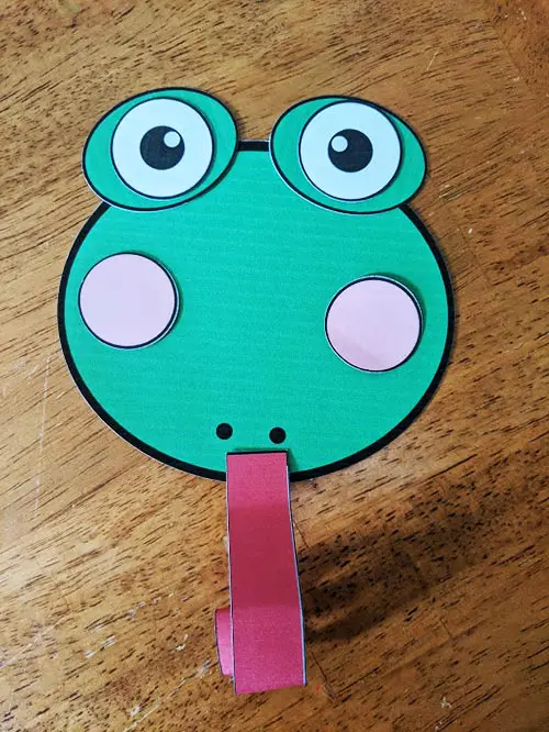 Paper cut outs for making frog face craft with curled tongue.