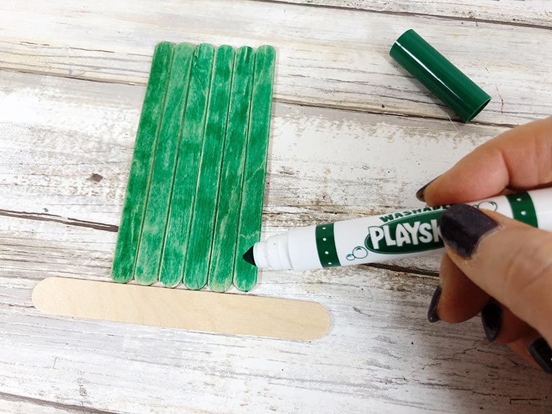 Coloring popsicle sticks with green marker.