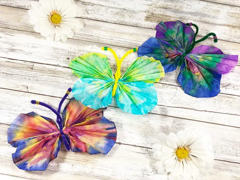 Three coffee filter butterflies in different colors laying next to each other.