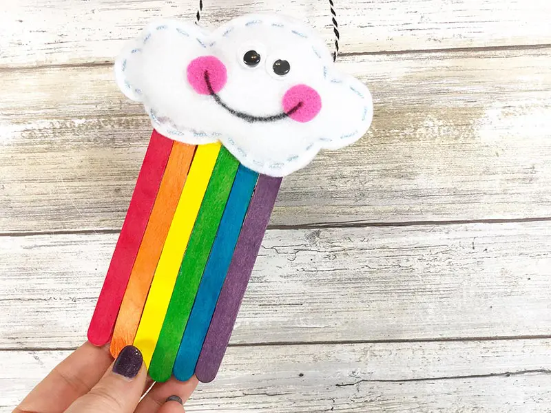 Hand holding up completed rainbow popsicle stick craft.