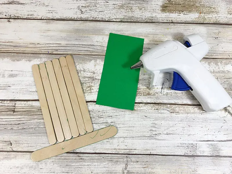 Popsicle sticks arranged to look like a hat, green paper, and glue gun.