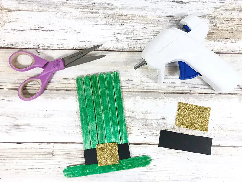 Gluing black and gold paper to green popsicle stick hat.