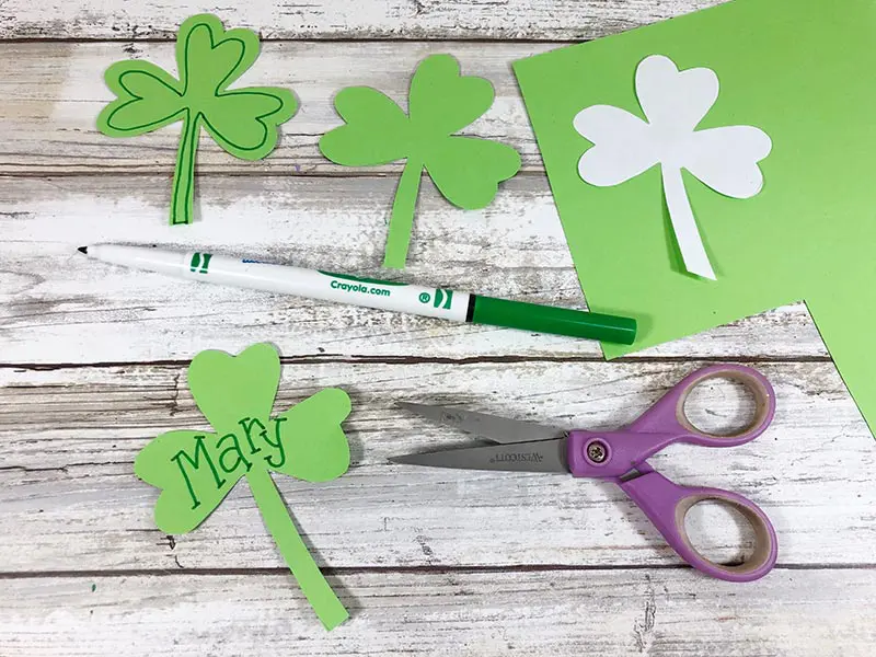 Shamrock cutouts and template laying on green paper. One shamrock says Mary.