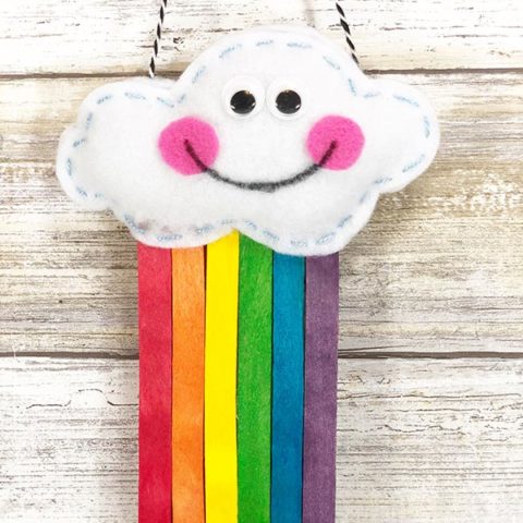 Stuffed cloud with smiley face and rainbow colored popsicle sticks coming out the bottom is hanging up.