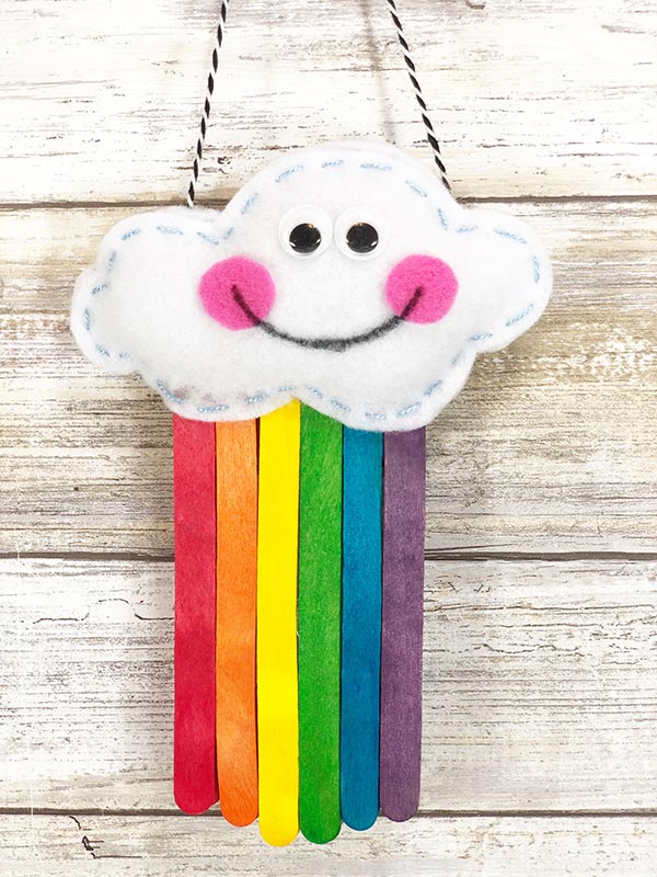 Stuffed cloud with smiley face and rainbow colored popsicle sticks coming out the bottom is hanging up.