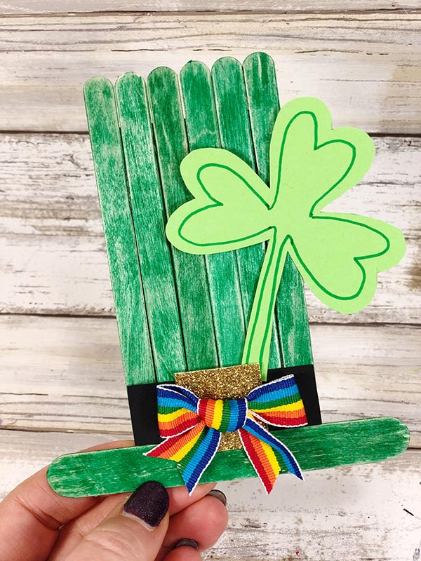 Hand holding completed green leprechaun hat made from popsicle sticks.