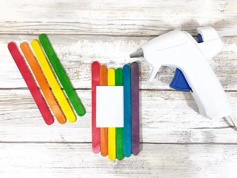 Popsicle sticks arranged in rainbow color order next to glue gun.